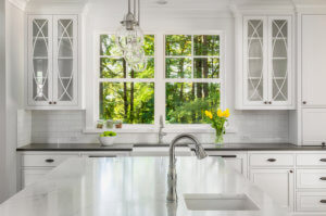Kitchen in new home with island, two sinks, window view of vibrant green trees, pendant lights, and cabinetry